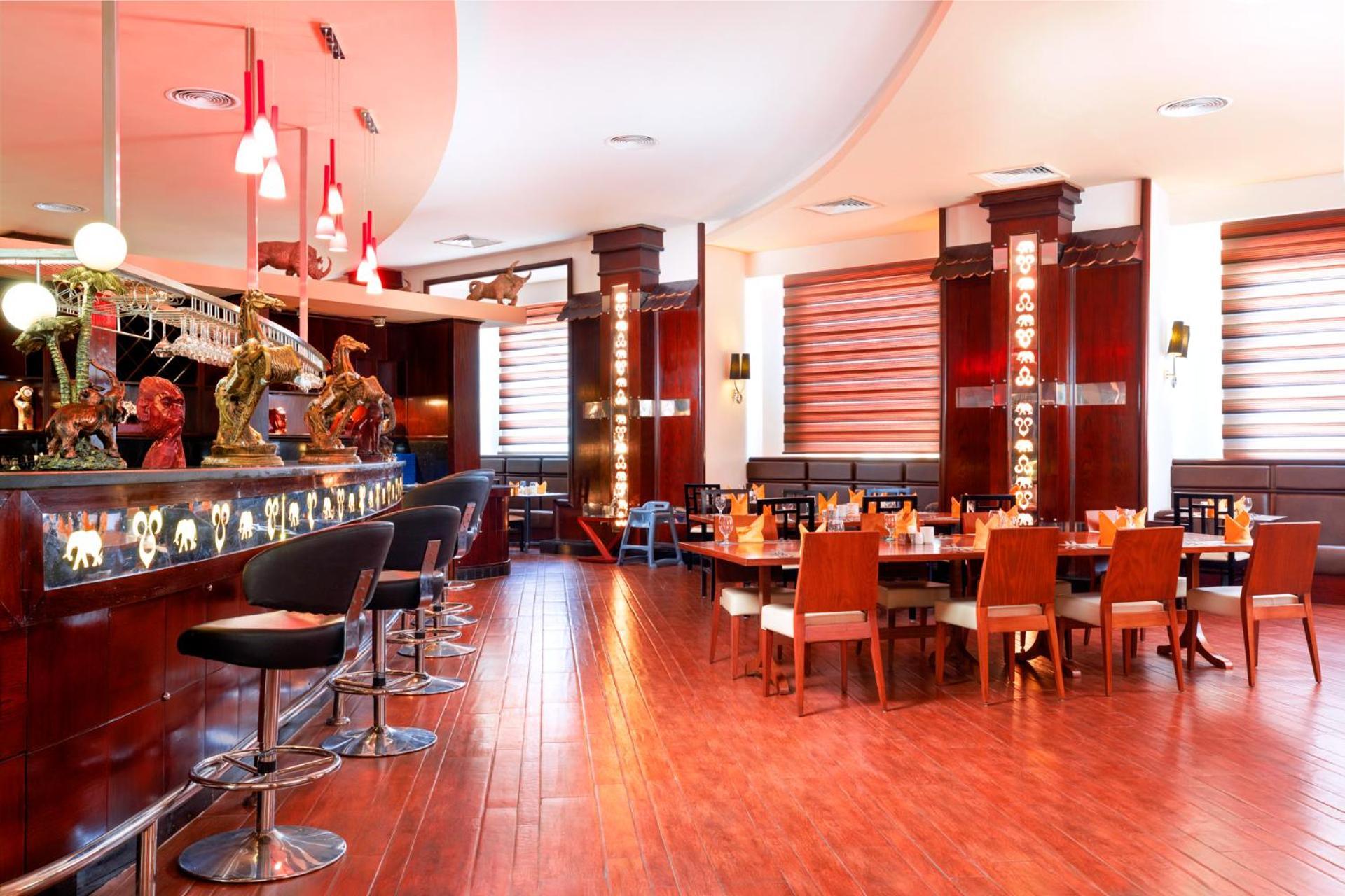 Hotel Pickalbatros Royal Moderna Sharm "Aqua Park" Exteriér fotografie The photo shows the interior of a restaurant. It features a sleek, modern design with wooden floors and a warm color palette. On the left, there is a bar area with high stools, and the bar itself is illuminated with decorative lights. The seating inc