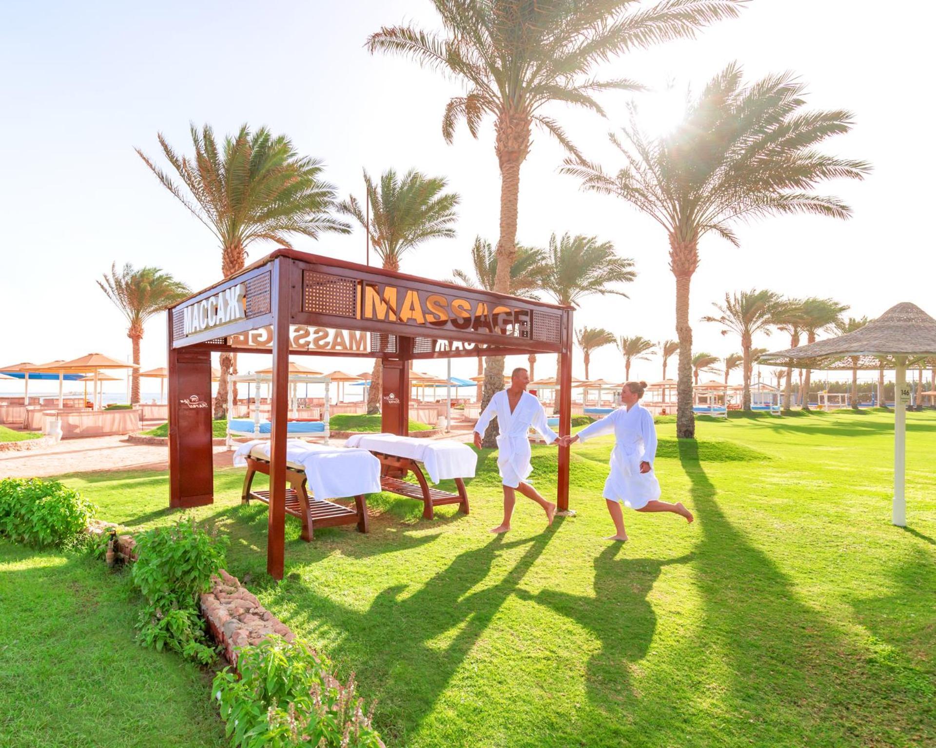 Hotel Pickalbatros Royal Moderna Sharm "Aqua Park" Exteriér fotografie The photo shows a serene outdoor spa area, featuring a massage pavilion with a sign that reads "MASAGE." There are two individuals in white robes, appearing to enjoy a light-hearted moment while walking towards the pavilion. Surrounding the pavilion 