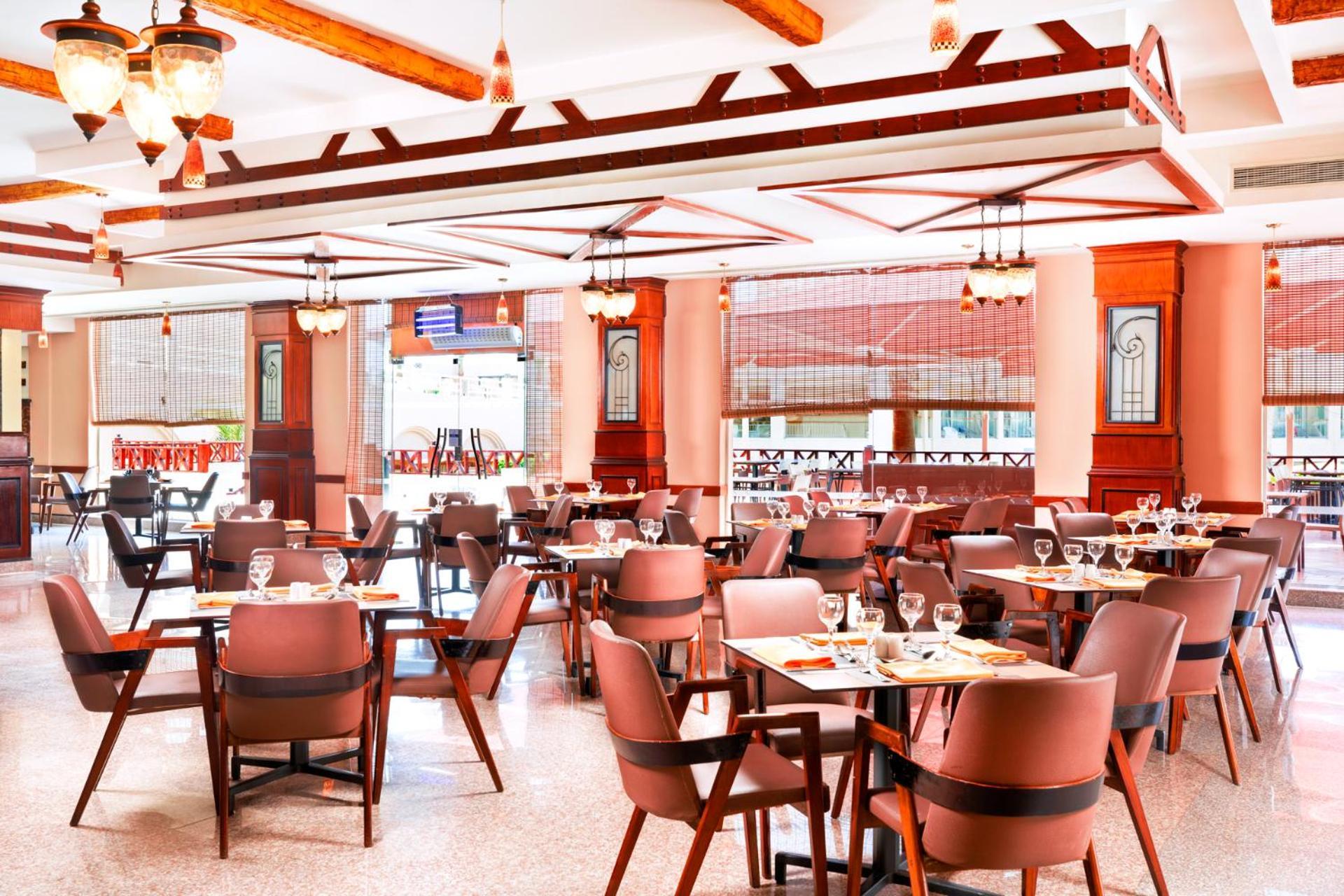Hotel Pickalbatros Royal Moderna Sharm "Aqua Park" Exteriér fotografie The photo shows the interior of a restaurant. It features a spacious dining area with several tables set for patrons, each equipped with cutlery and glassware. The decor includes wooden beams and pendant lighting, creating a warm and inviting atmosph