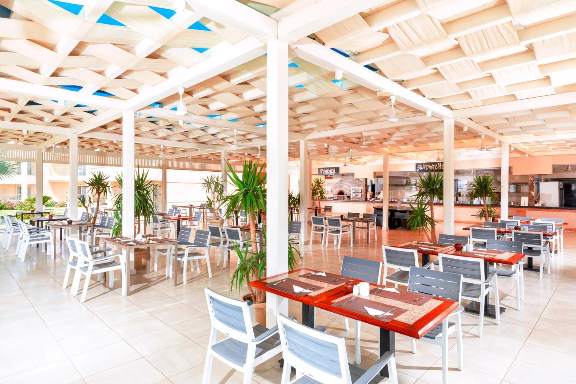 Hotel Pickalbatros Royal Moderna Sharm "Aqua Park" Exteriér fotografie The photo depicts the interior of a modern restaurant. The space features a contemporary design with wooden tables and light-colored chairs arranged throughout the dining area. The ceiling has a unique, textured pattern, enhancing the airy and open f