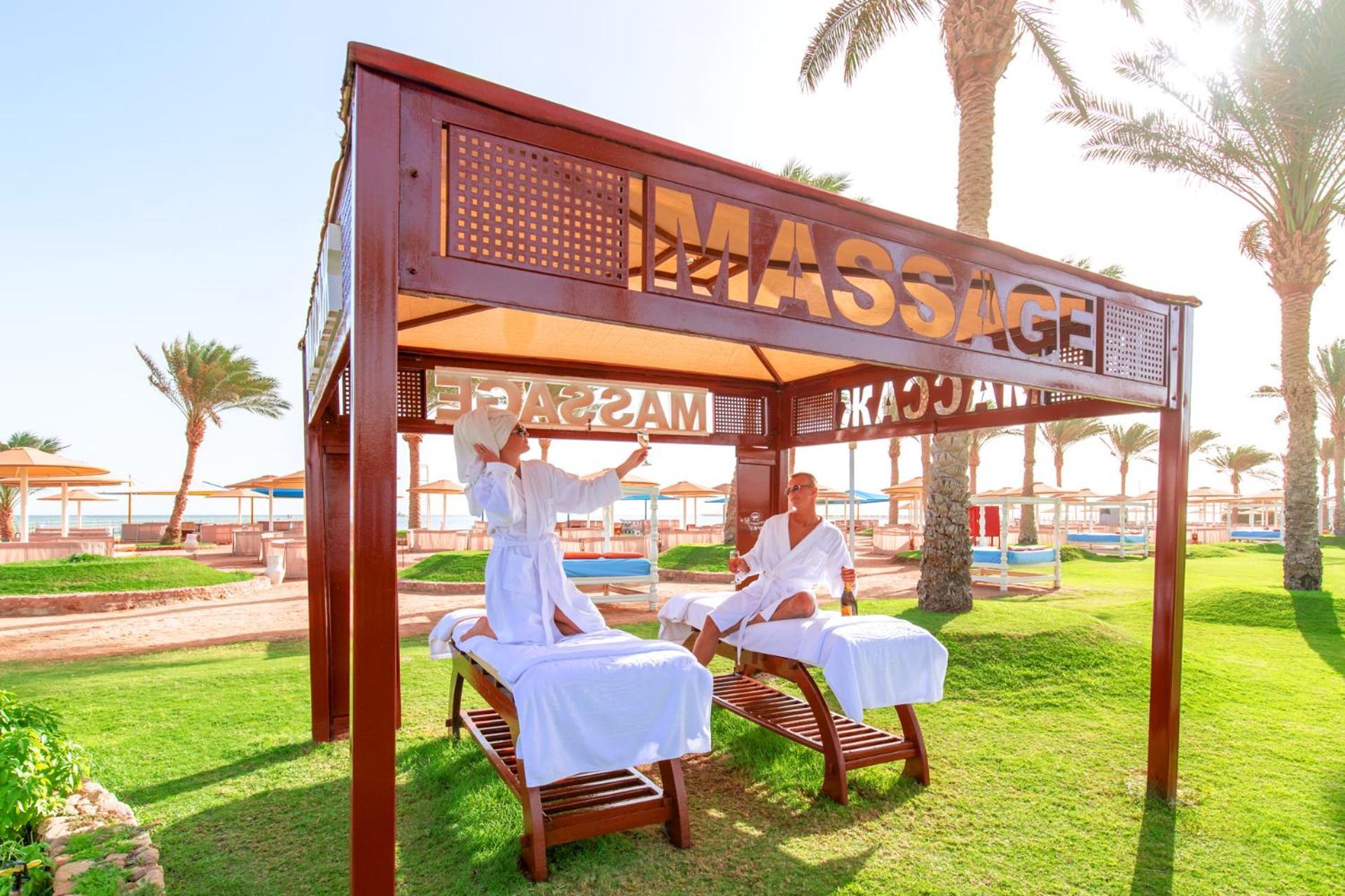 Hotel Pickalbatros Royal Moderna Sharm "Aqua Park" Exteriér fotografie The photo shows a massage area set up in a sunny outdoor environment. There are two massage tables under a wooden canopy with the word "MASSAGE" prominently displayed. Two individuals, dressed in white robes, appear to be engaged in a massage session
